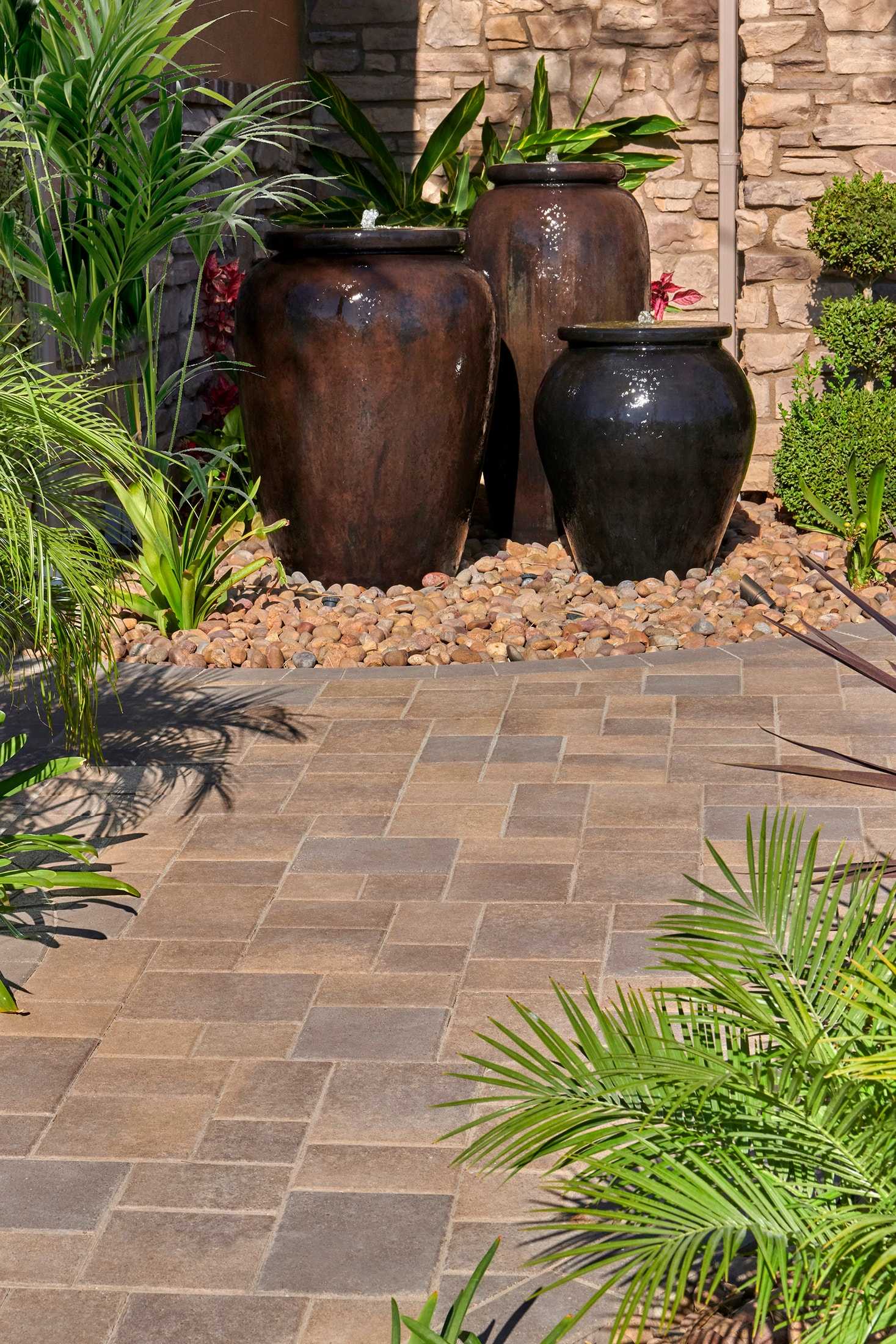 Brown and tan patio pavers beside planting and dark glazed vessels.